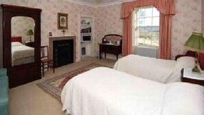 Une chambre avec deux lits, un miroir, une cheminée, un bureau et une fenêtre avec des rideaux.