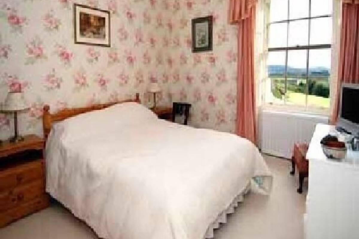 A bedroom with a bed, a desk, a chair, and a window with a view.