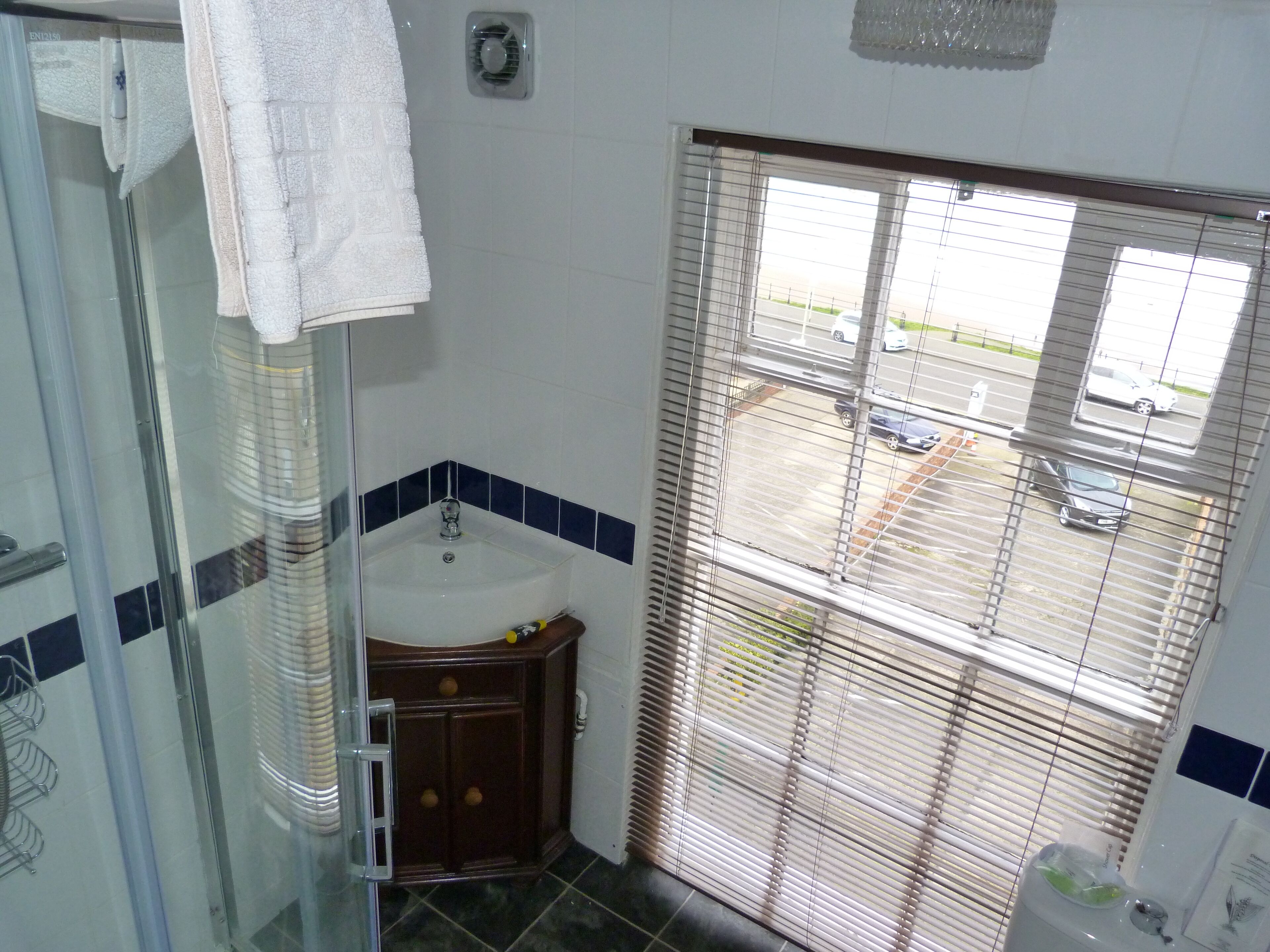Een badkamer met een douchecabine van glas, een wastafel met spiegel en een raam met jaloezieën.