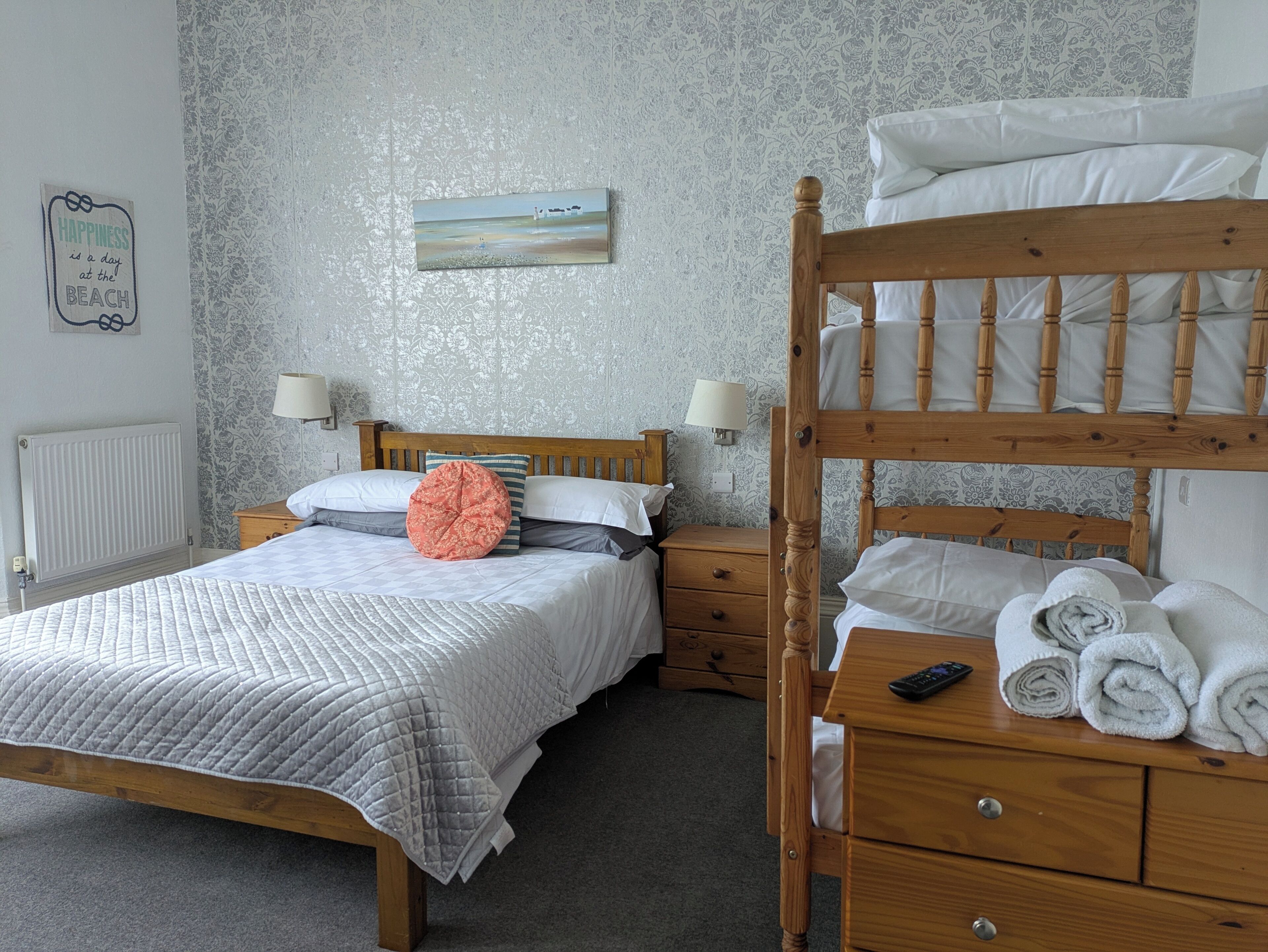 A bedroom with a bunk bed, a bedside table with a lamp, a nightstand, and a wall with a decorative piece.