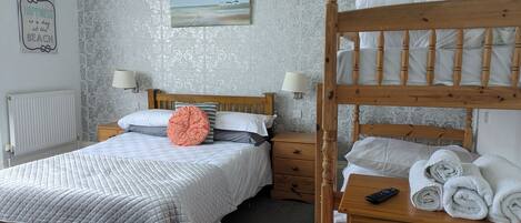 A bedroom with a bunk bed, a bedside table with a lamp, a nightstand, and a wall with a decorative piece.