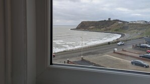 A coastal road with a view of the sea and a hill with buildings. - The Kenton (Scarborough)