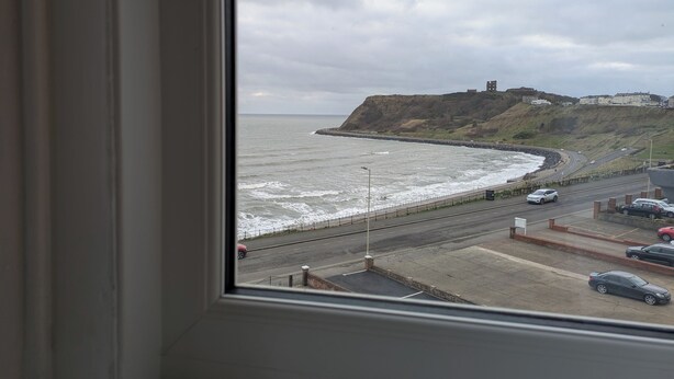 A coastal road with a view of the sea and a hill with buildings. - The Kenton (Scarborough)