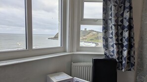 A room with a bay window overlooking the sea, a radiator, and two white appliances. - The Kenton (Scarborough)