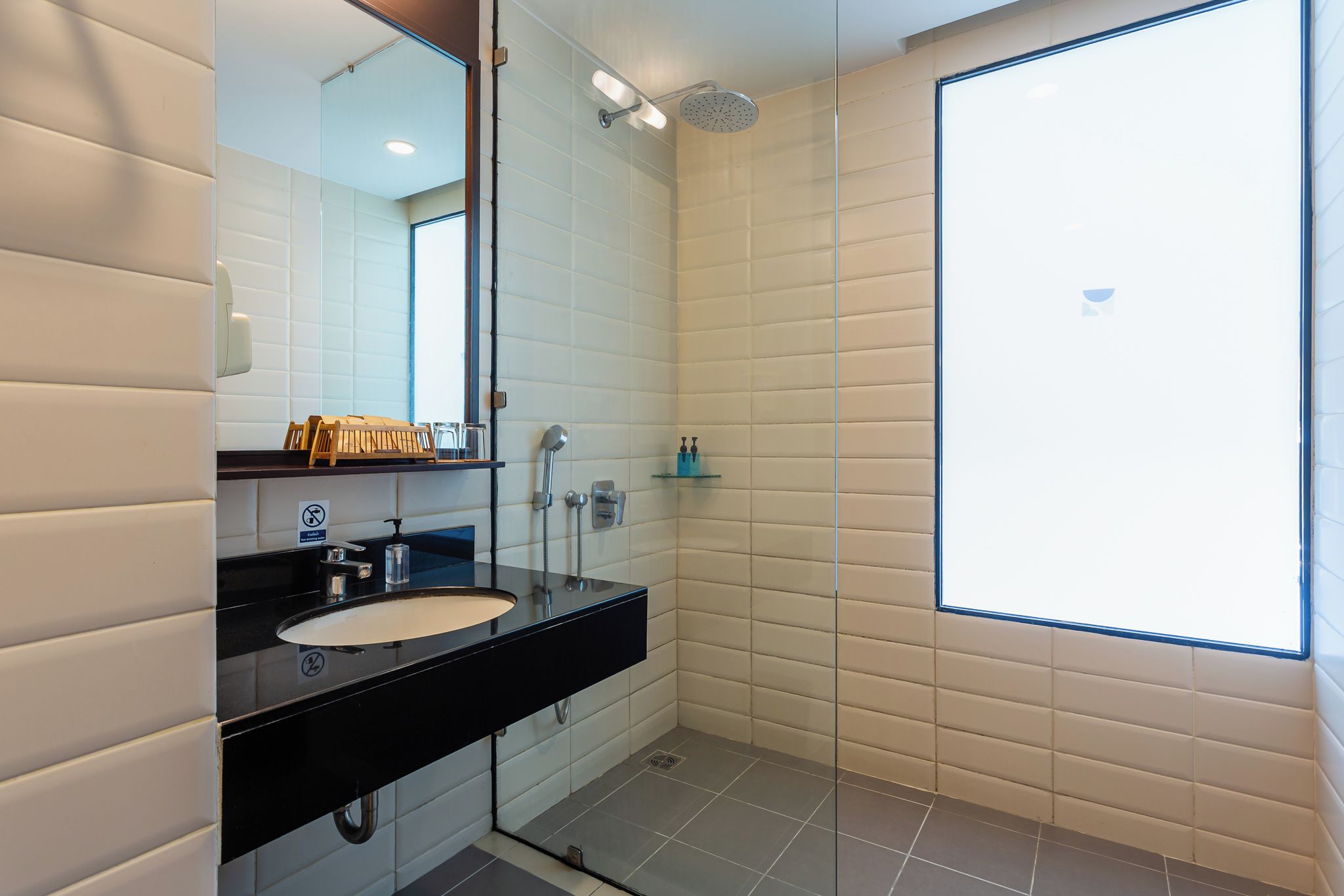 Un baño moderno con un lavabo negro, un espejo, una ducha y una ventana.