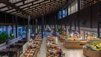 A spacious indoor dining area with multiple tables and chairs, a buffet counter with various food items, and large windows allowing natural light.