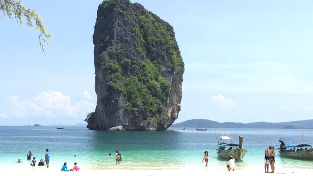 A beach with clear turquoise water, a large rock formation, and several boats. - Deevana Plaza Krabi (Krabi)