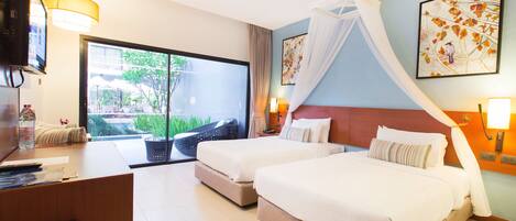 A hotel room with two beds, a desk, a TV, and a large window with a view of greenery.