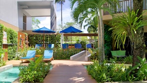 A pool area with lounge chairs and umbrellas, surrounded by greenery and a wooden deck. - Deevana Plaza Krabi (Krabi)