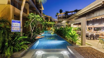 A pool area with a sign detailing pool rules, surrounded by lush greenery and a modern building structure.