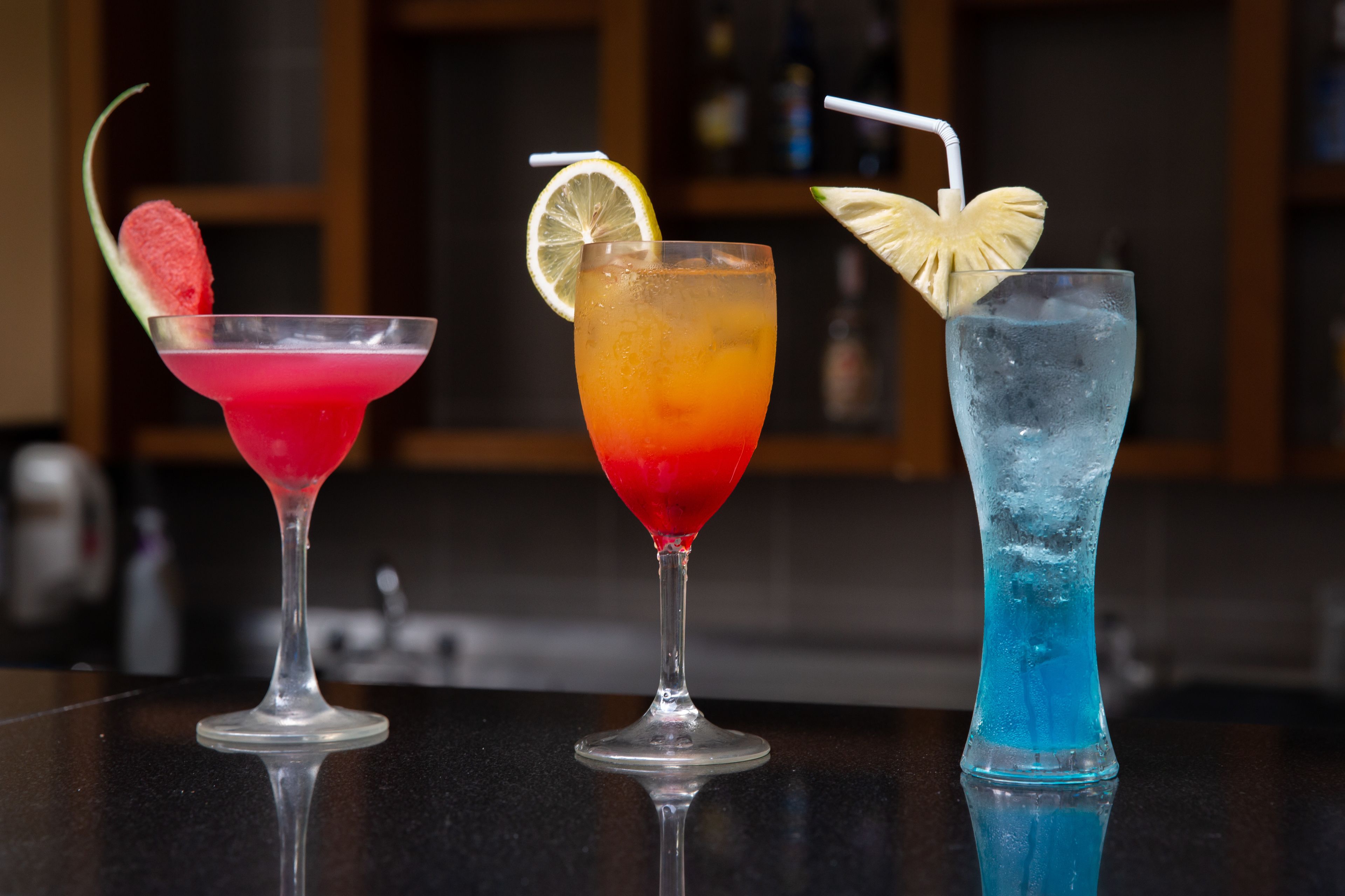 Três cocktails em um balcão de bar, com o fundo desfocado.