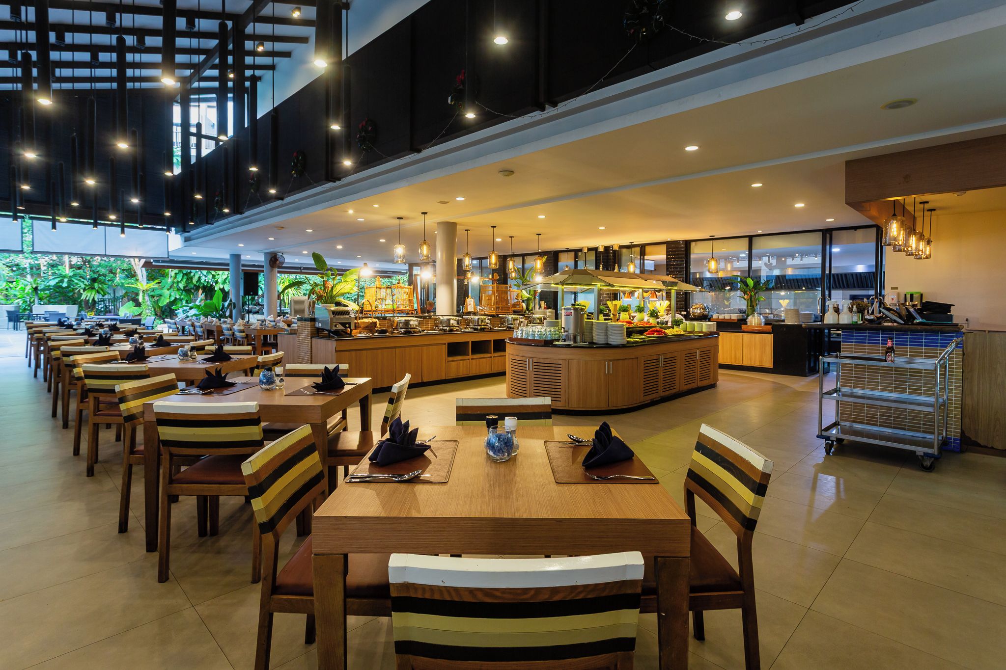 Een ruime eethoek met meerdere tafels en stoelen, een centraal buffet en een keuken op de achtergrond.