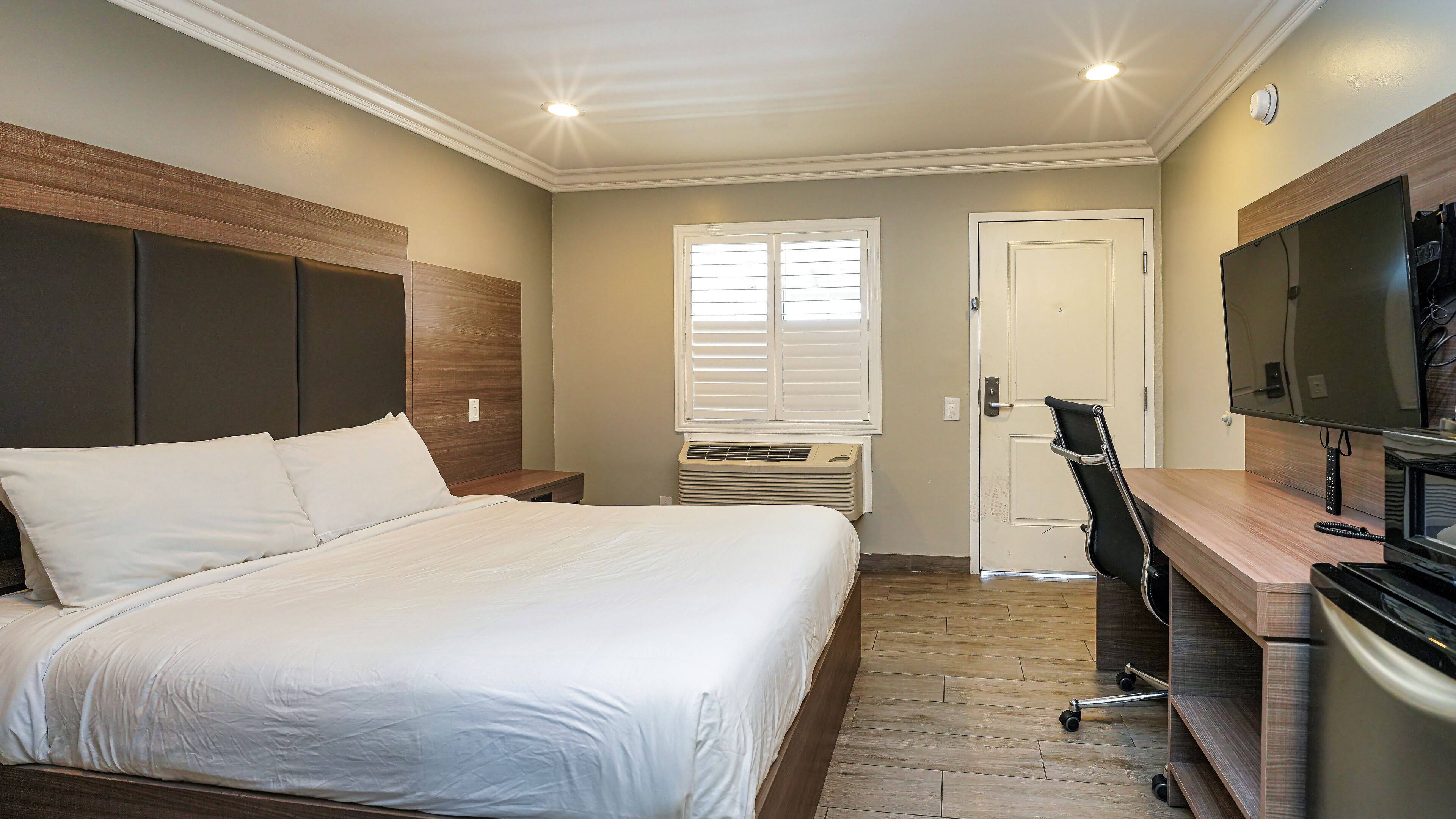 A hotel room with a large bed, a desk with a computer, a TV, and a window with blinds.