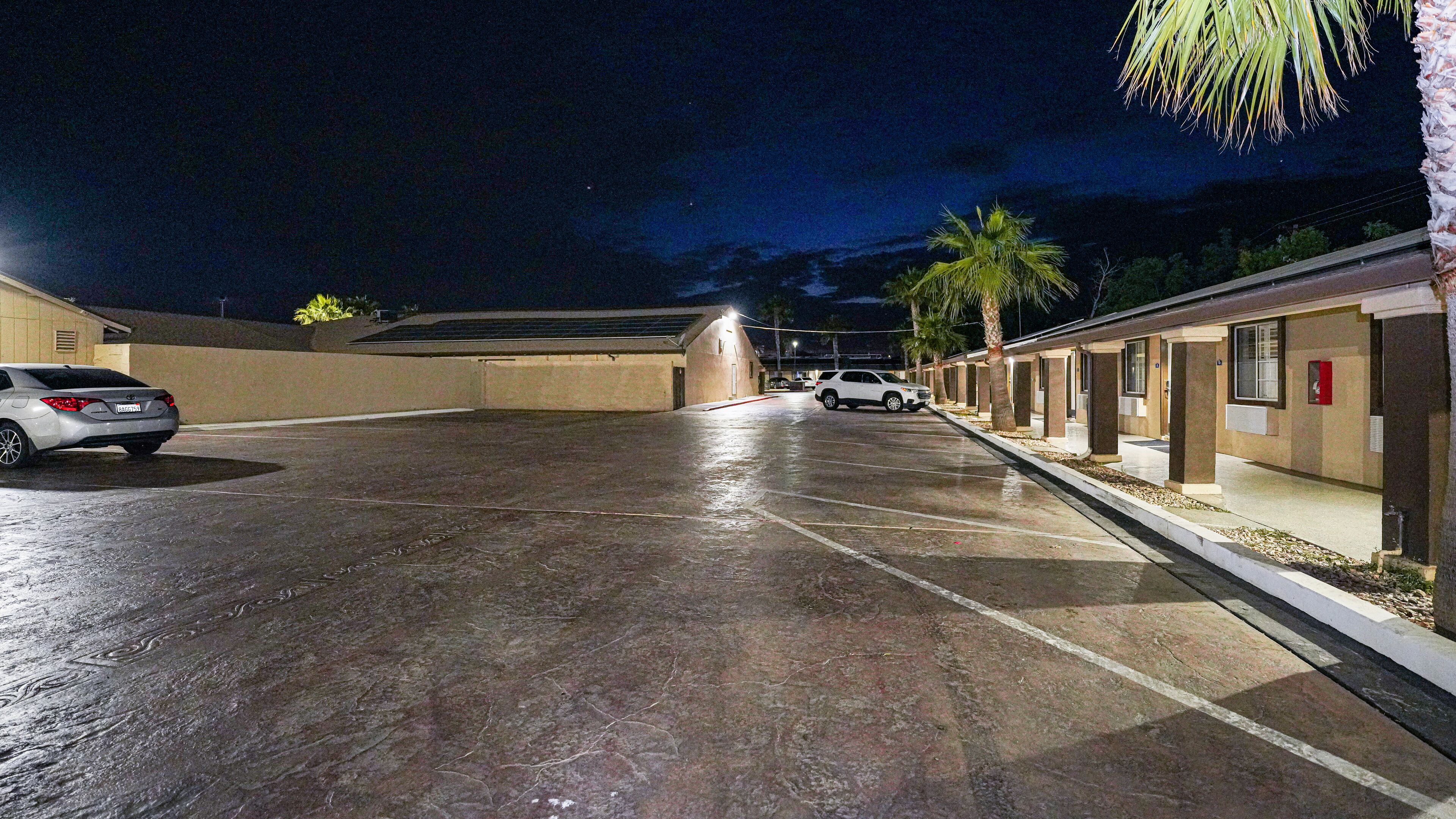 A parking lot with a building in the background, a car parked on the left, and palm trees along the right side.