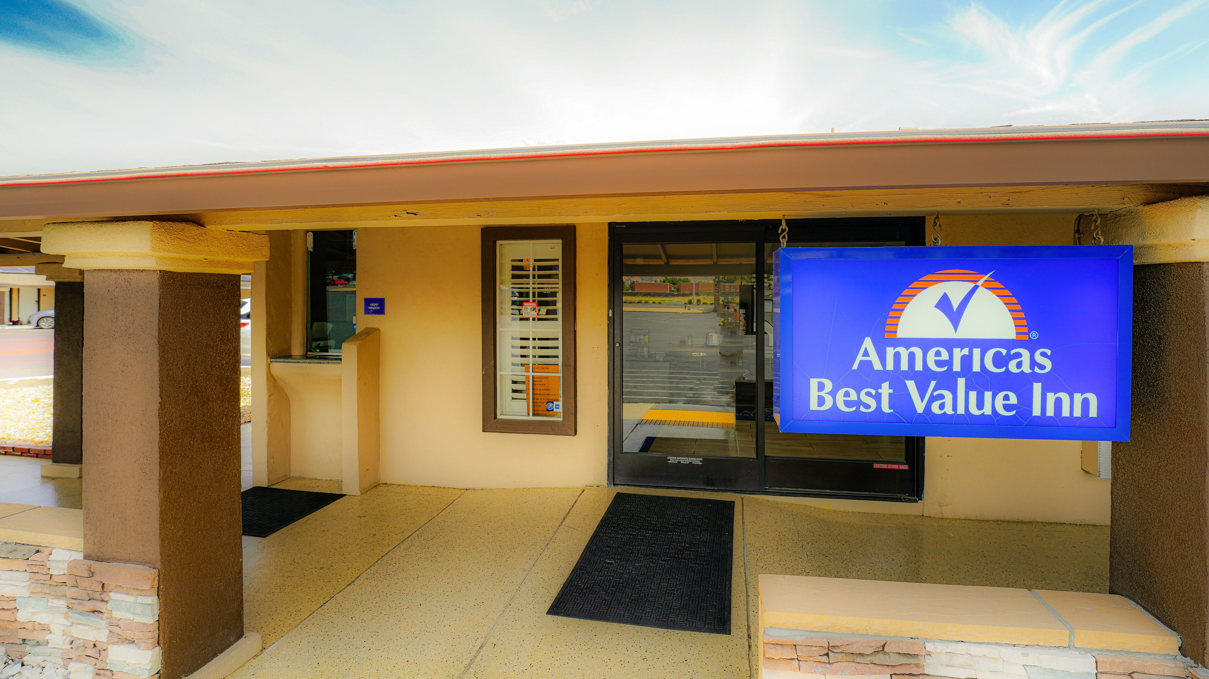 Exterior de un Americas Best Value Inn con entrada despejada, un letrero azul y una ventana con persianas visibles.