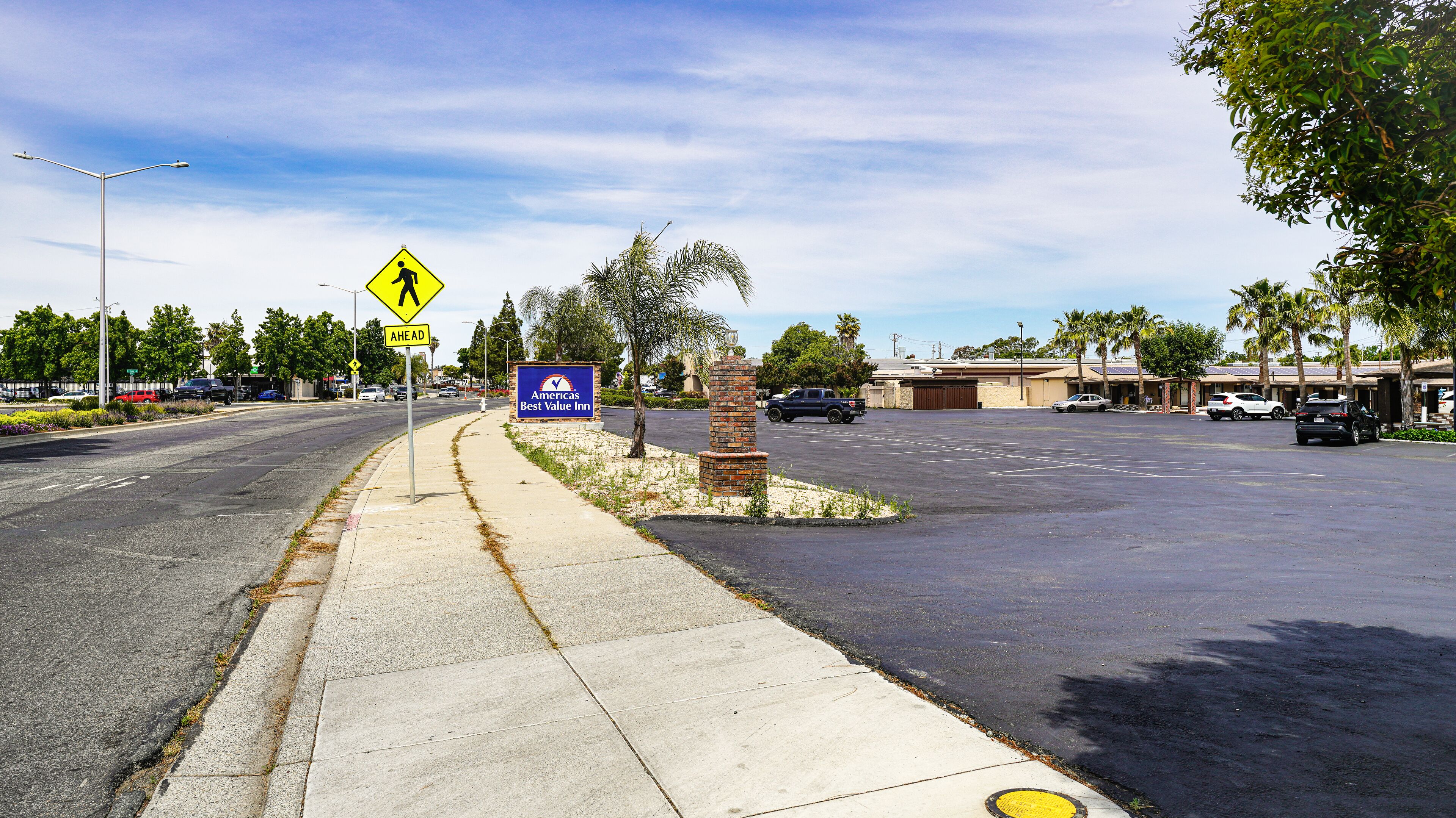 A parking lot with a pedestrian crossing sign, a blue sign with 'America's Best Value Inn' text, and a brick pillar.