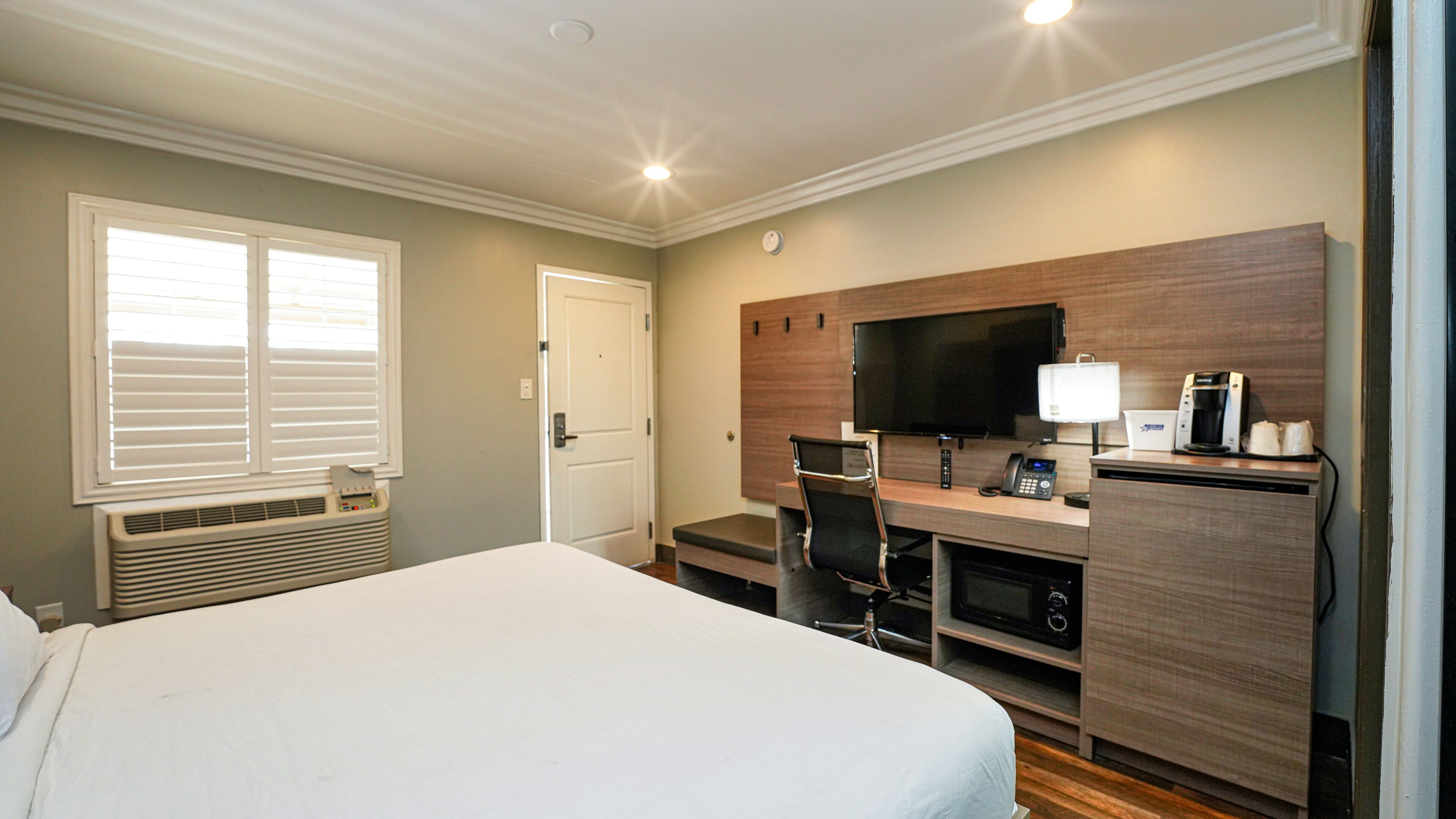 Una habitación de hotel con una cama grande, un escritorio con computadora, un televisor y una cafetera.