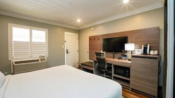 Una habitación de hotel con una cama grande, un escritorio con computadora, un televisor y una cafetera.
