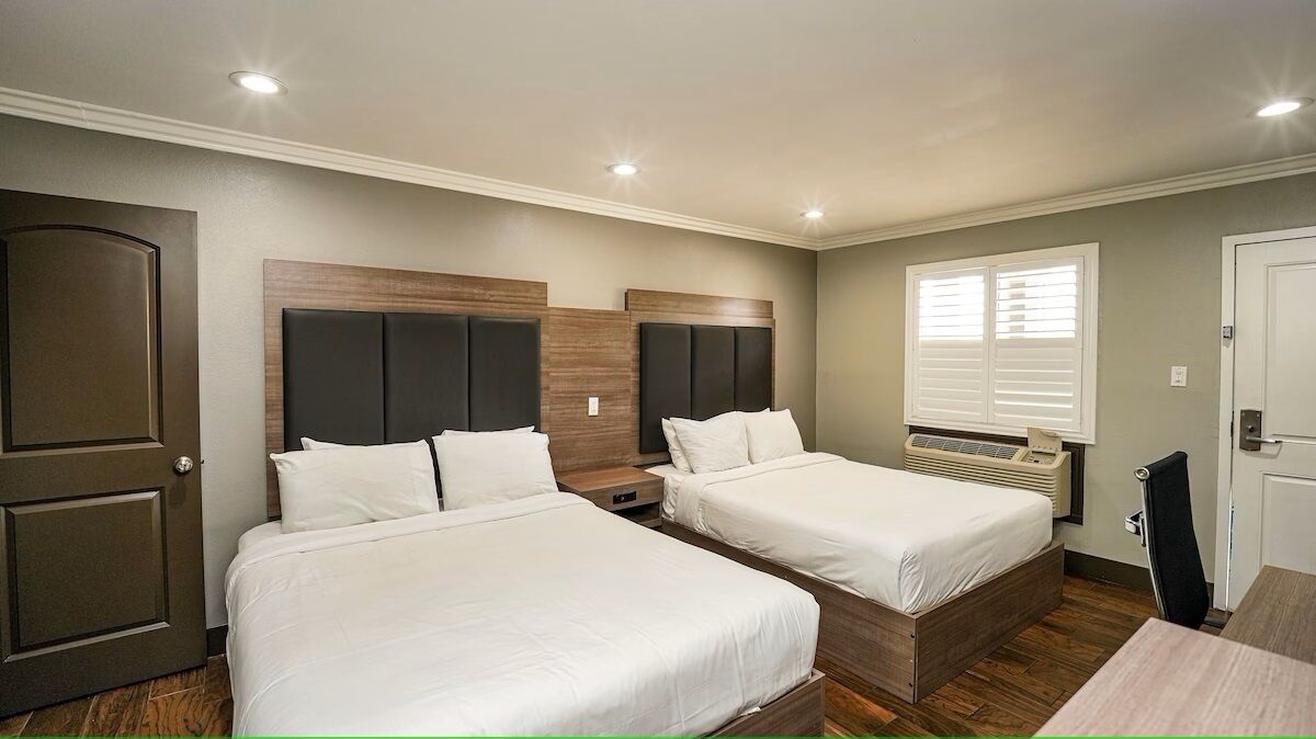 Une chambre avec deux lits, un radiateur, une fenêtre avec des stores et une porte.