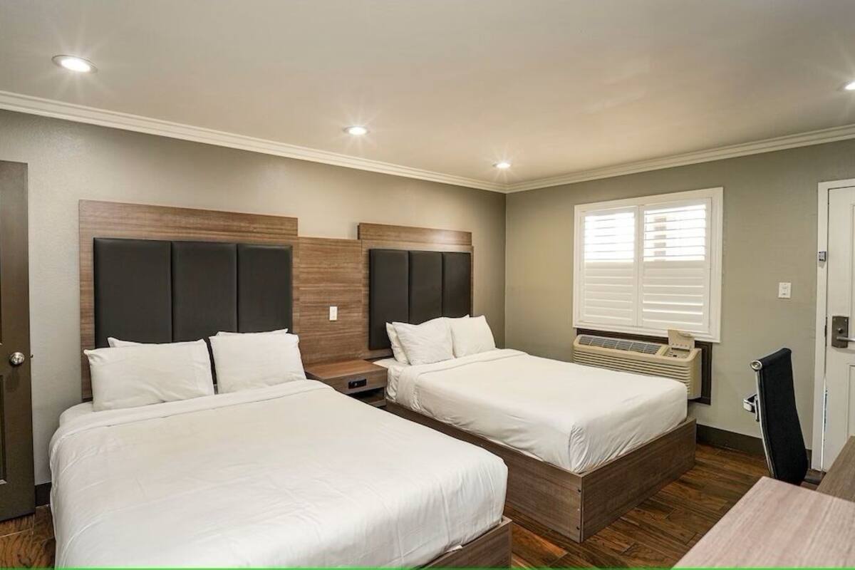 Une chambre avec deux lits, un radiateur, une fenêtre avec des stores et une porte.