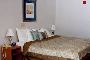 A neatly made bed with a patterned bedspread, two bedside lamps, a nightstand with a telephone, and a framed picture on the wall.