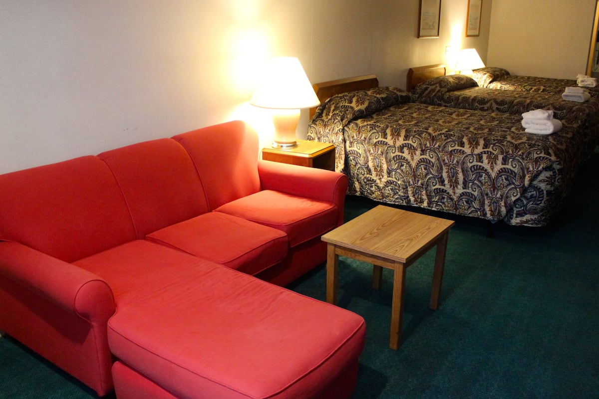 Une chambre d’hôtel avec un canapé rouge, une table en bois et un lit avec une literie à motifs.