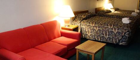 Une chambre d’hôtel avec un canapé rouge, une table en bois et un lit avec une literie à motifs.