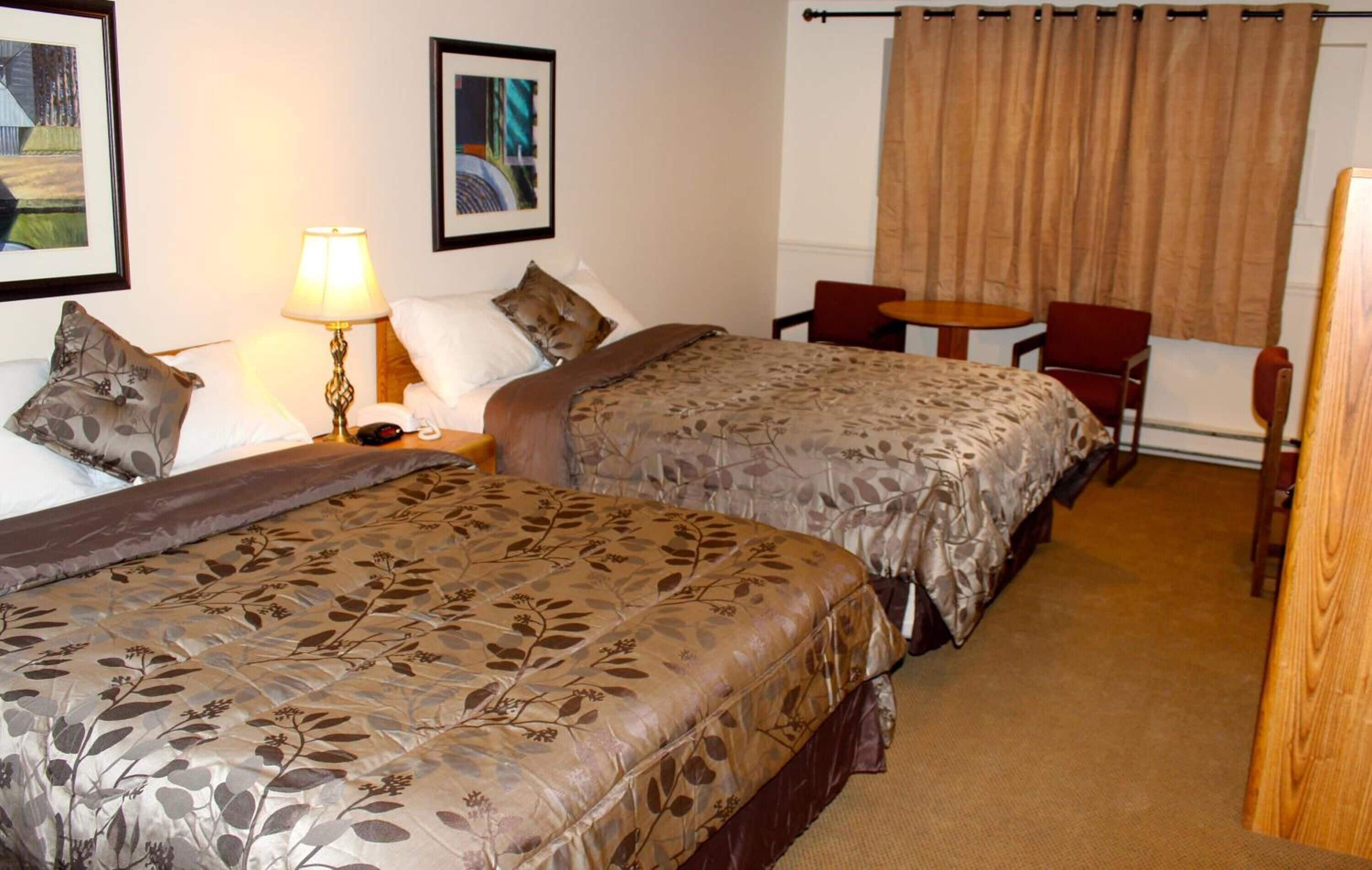 Habitación de hotel con dos camas, un escritorio, una silla, una lámpara y una ventana con cortinas.