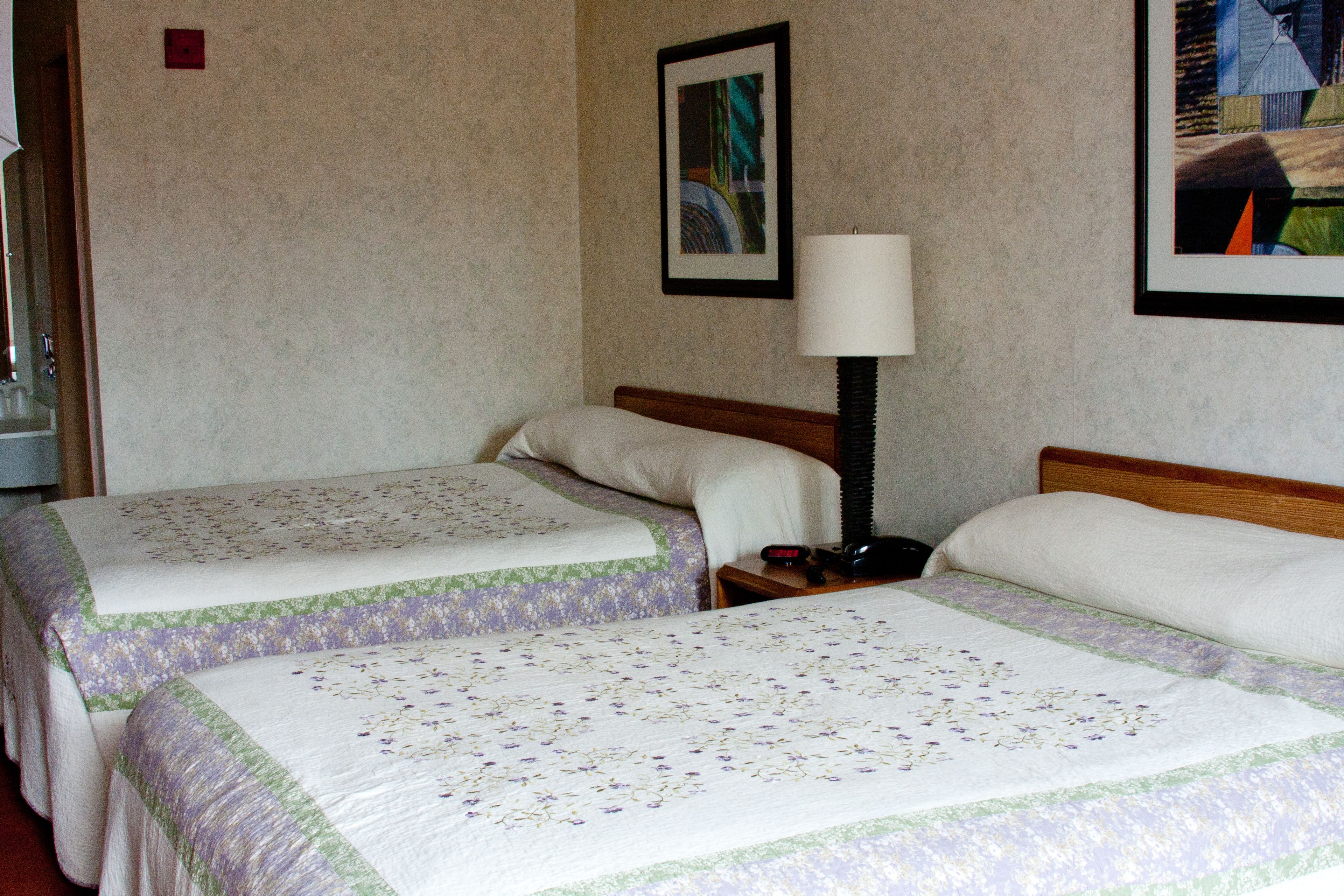 Ein Hotelzimmer mit zwei Betten, einem Nachttisch mit Lampe und einem gerahmten Bild an der Wand.