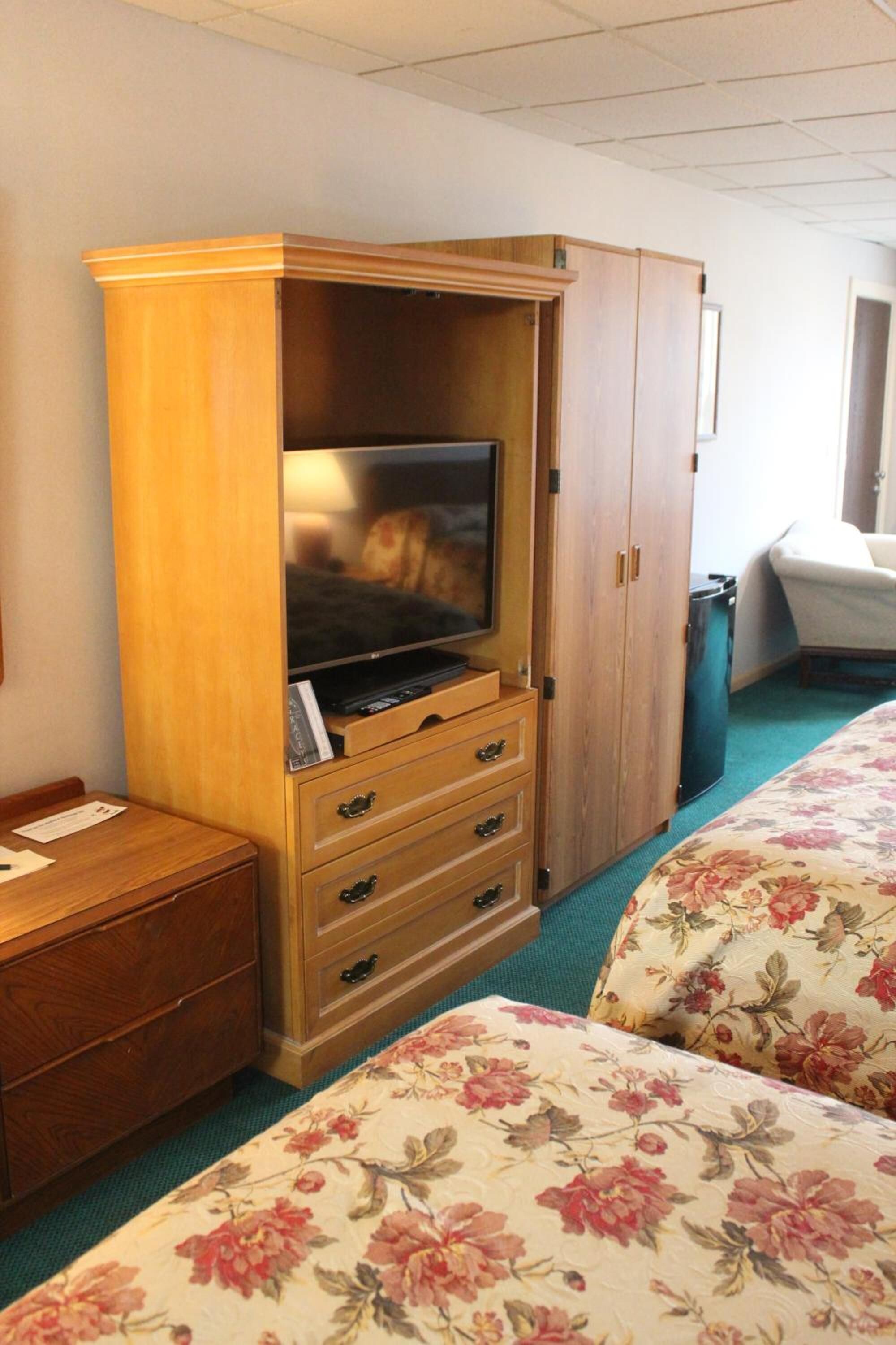 A hotel room with a wooden cabinet containing a television, a small wooden table, and a bed with floral bedding.