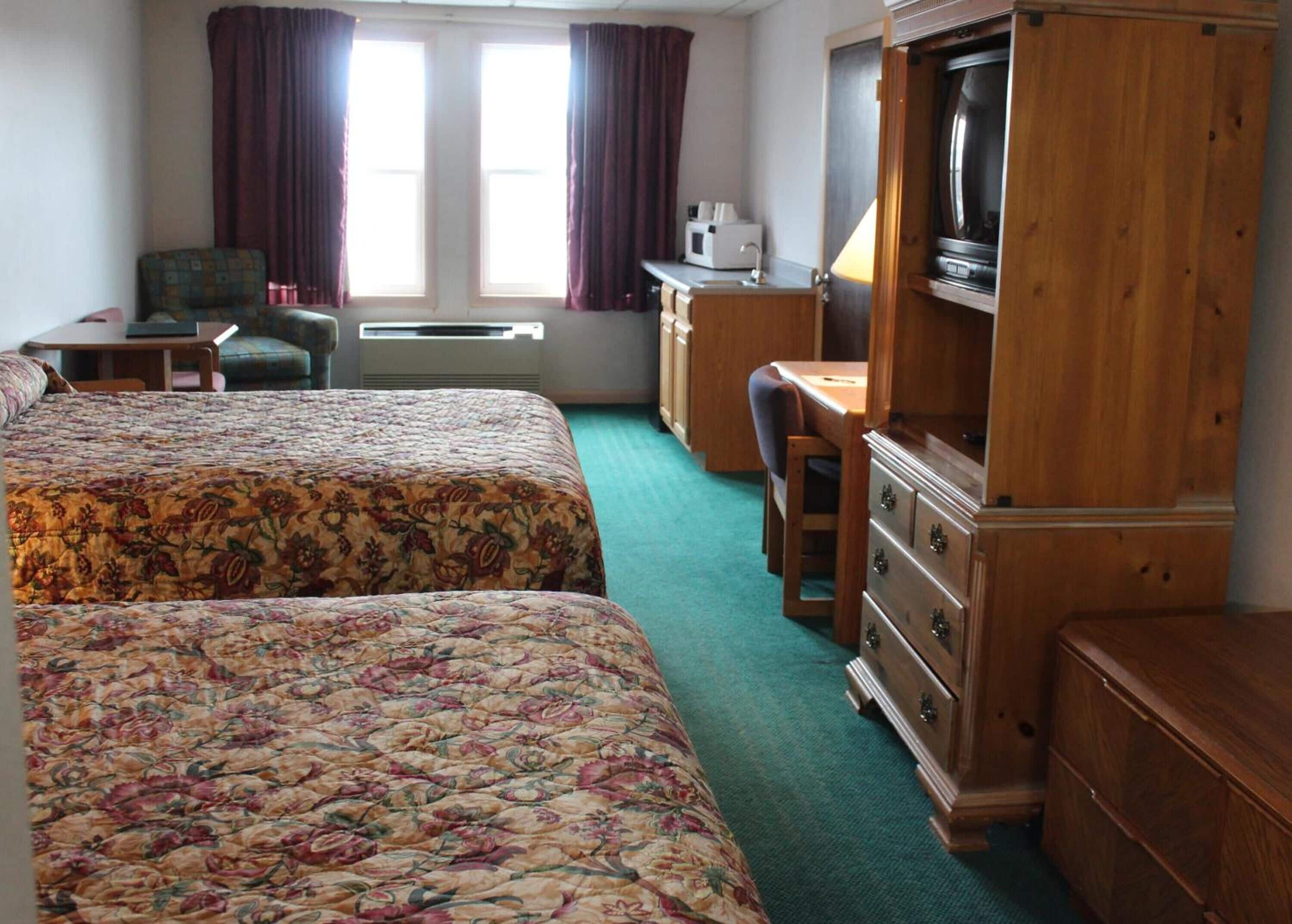 Una habitación de hotel con dos camas, un escritorio, una silla, un televisor y un armario.