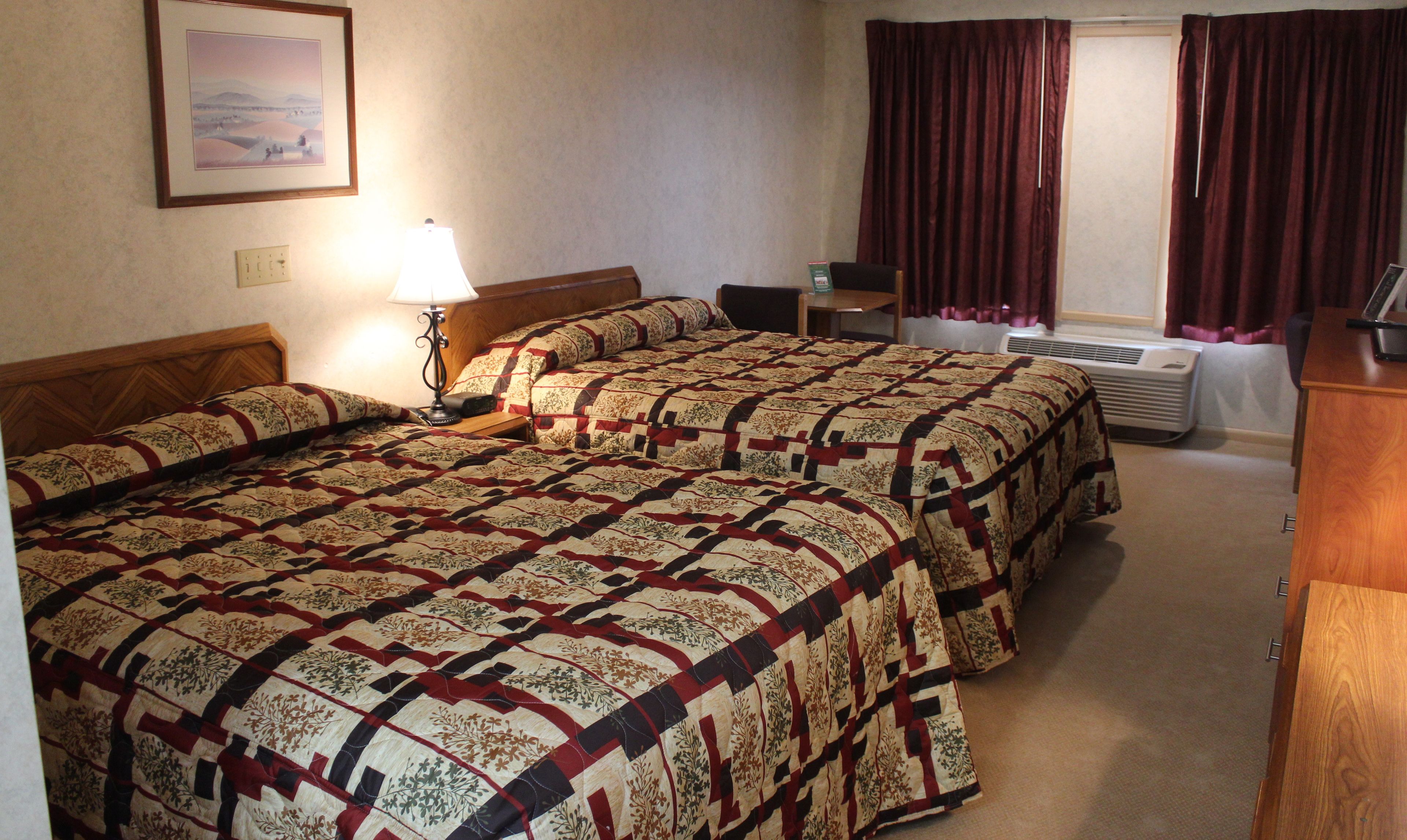 Een hotelkamer met twee bedden, een bureau, een lamp, een verwarming en een raam met gordijnen.