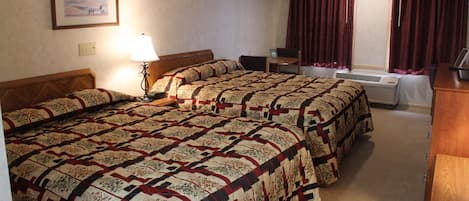 A hotel room with two beds, a desk, a lamp, a heater, and a window with curtains.