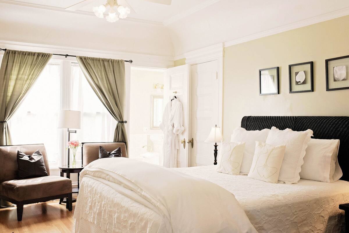 A hotel room with a large bed, a chair, a small table with a lamp, and a wardrobe.