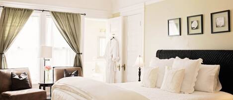 A hotel room with a large bed, a chair, a small table with a lamp, and a wardrobe.
