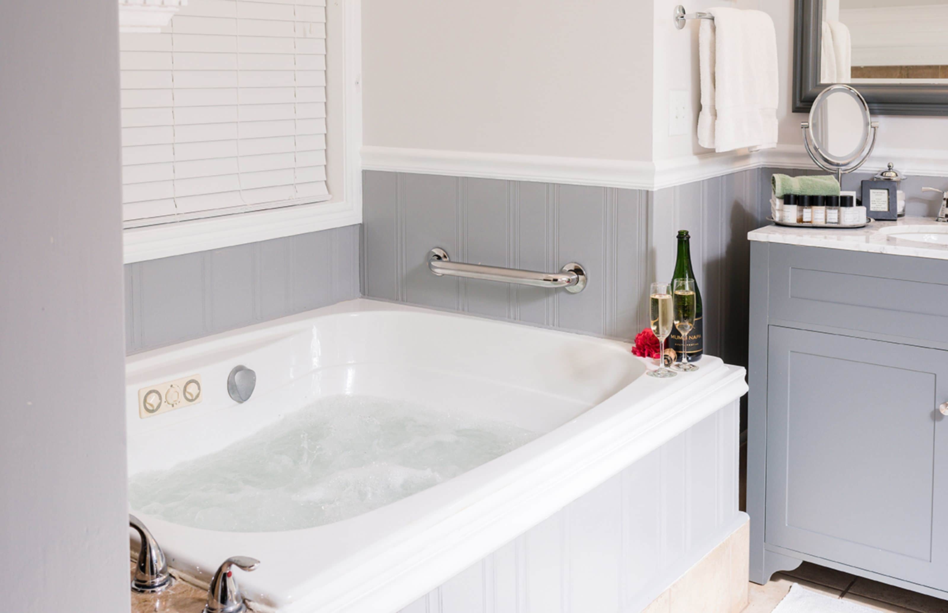 A bathroom with a white bathtub, a vanity with a mirror, and toiletries.