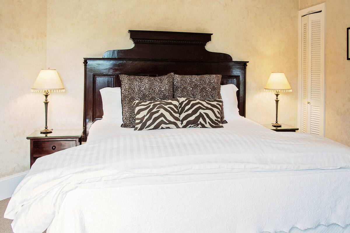 A neatly made bed with a zebra-patterned pillow, two bedside lamps, and a wooden headboard.