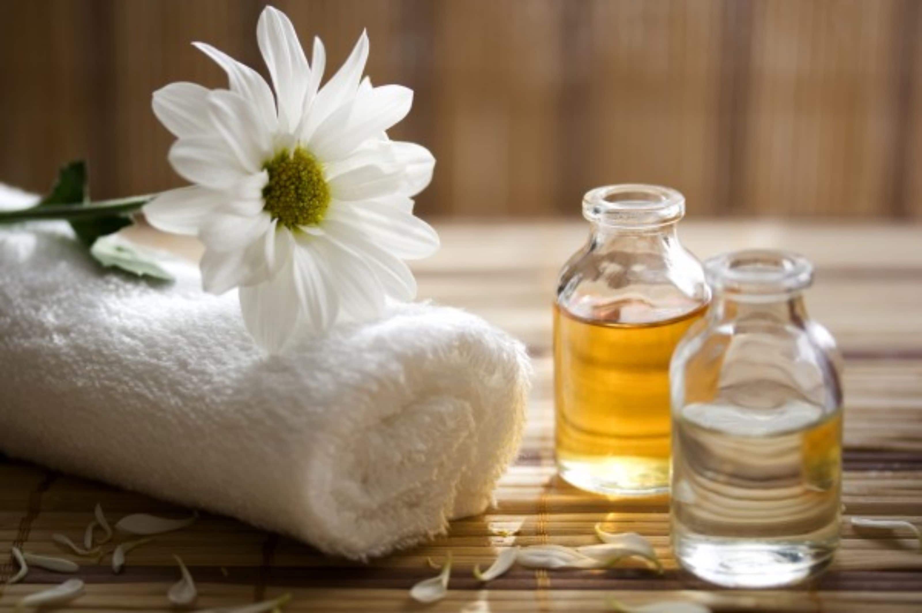 A white towel, a glass bottle with a yellow liquid, and a glass bottle with a clear liquid on a bamboo mat.