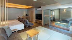 A modern hotel room with a large bed, a sofa, a small table, a TV, and a glass-enclosed balcony with a hot tub. - Hotel Okada (Hakone)