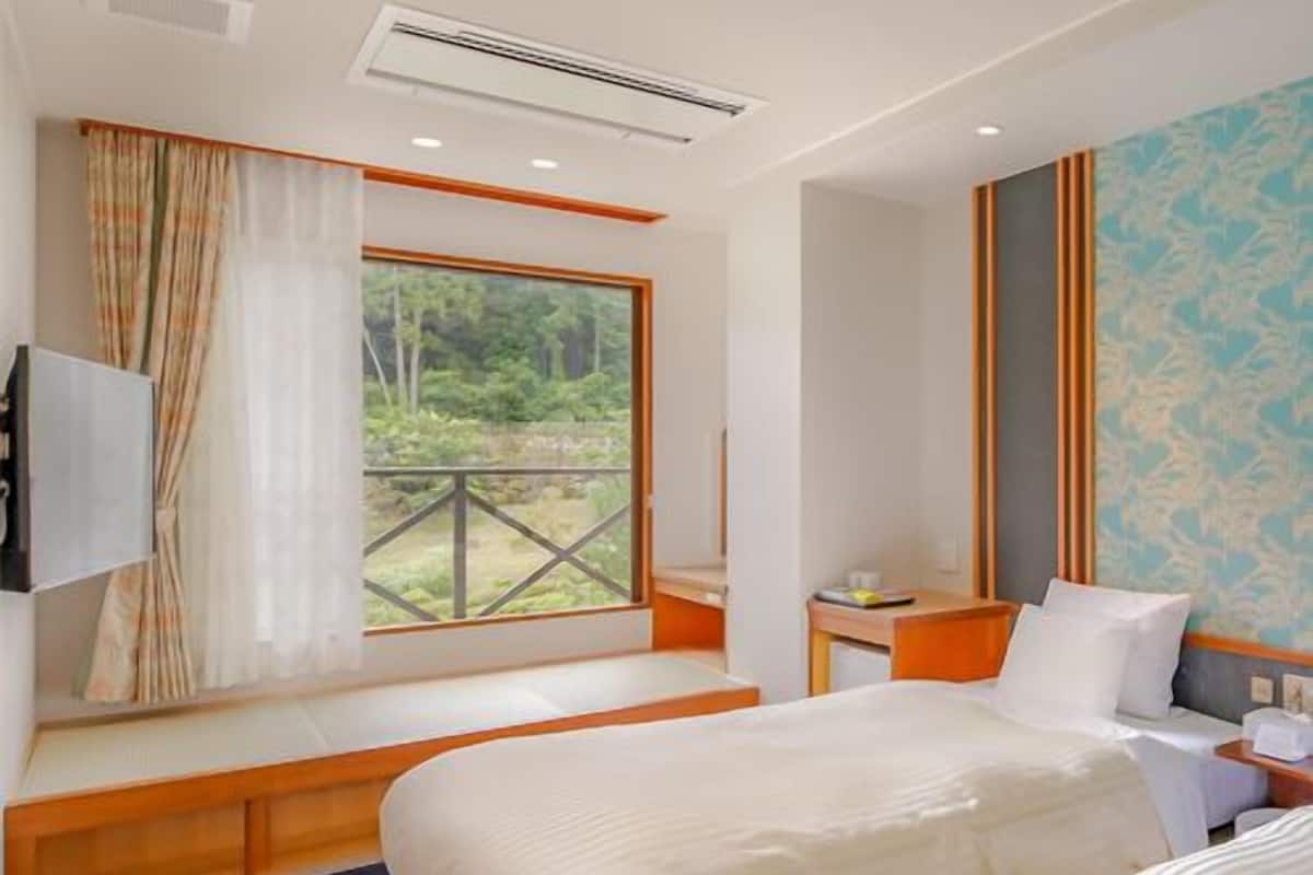 Una habitación de hotel con un ventanal grande, una cama, una mesita de noche y un televisor.