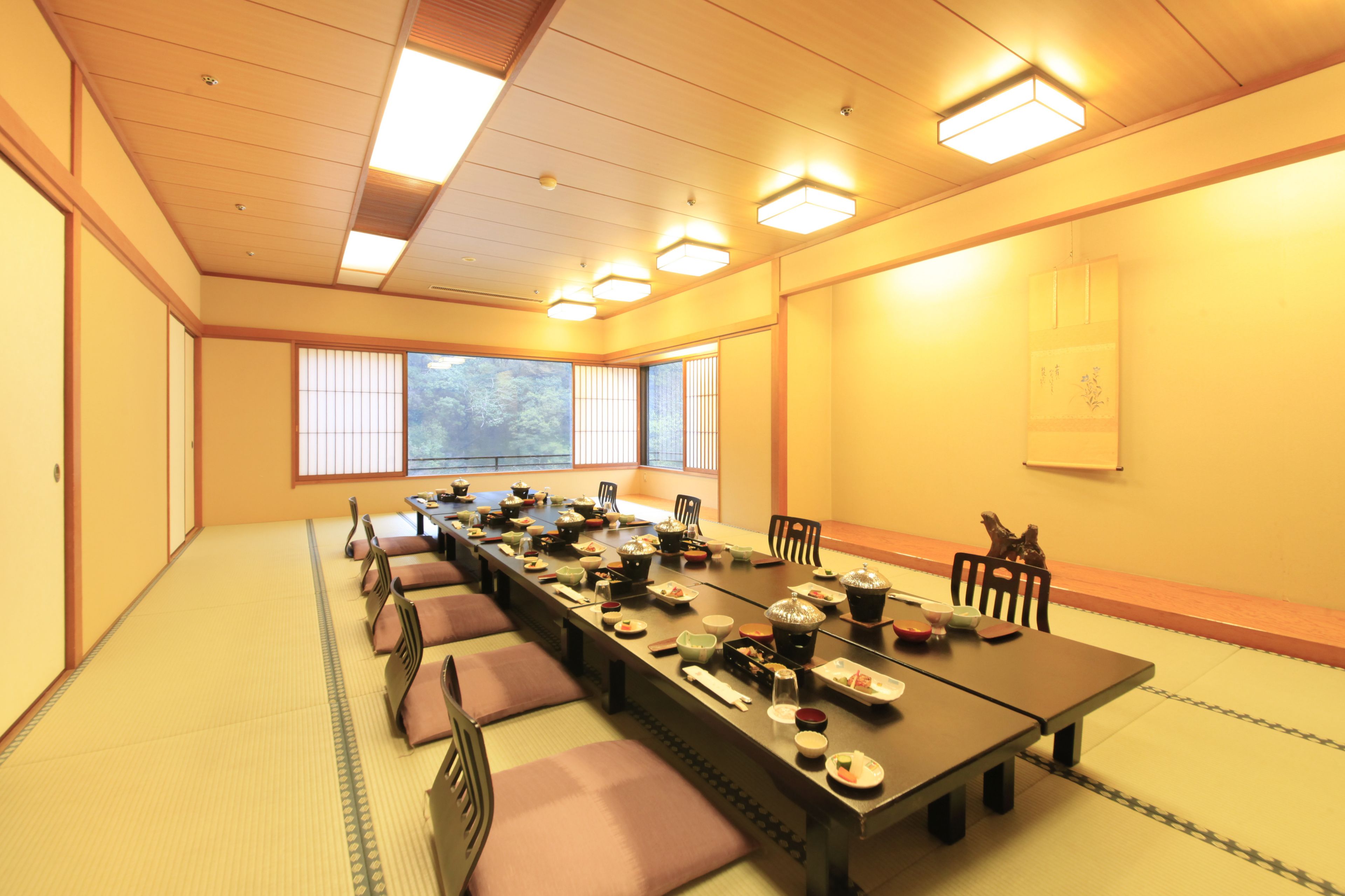 A traditional Japanese-style room with tatami mats, a long table set for a meal, and sliding doors.