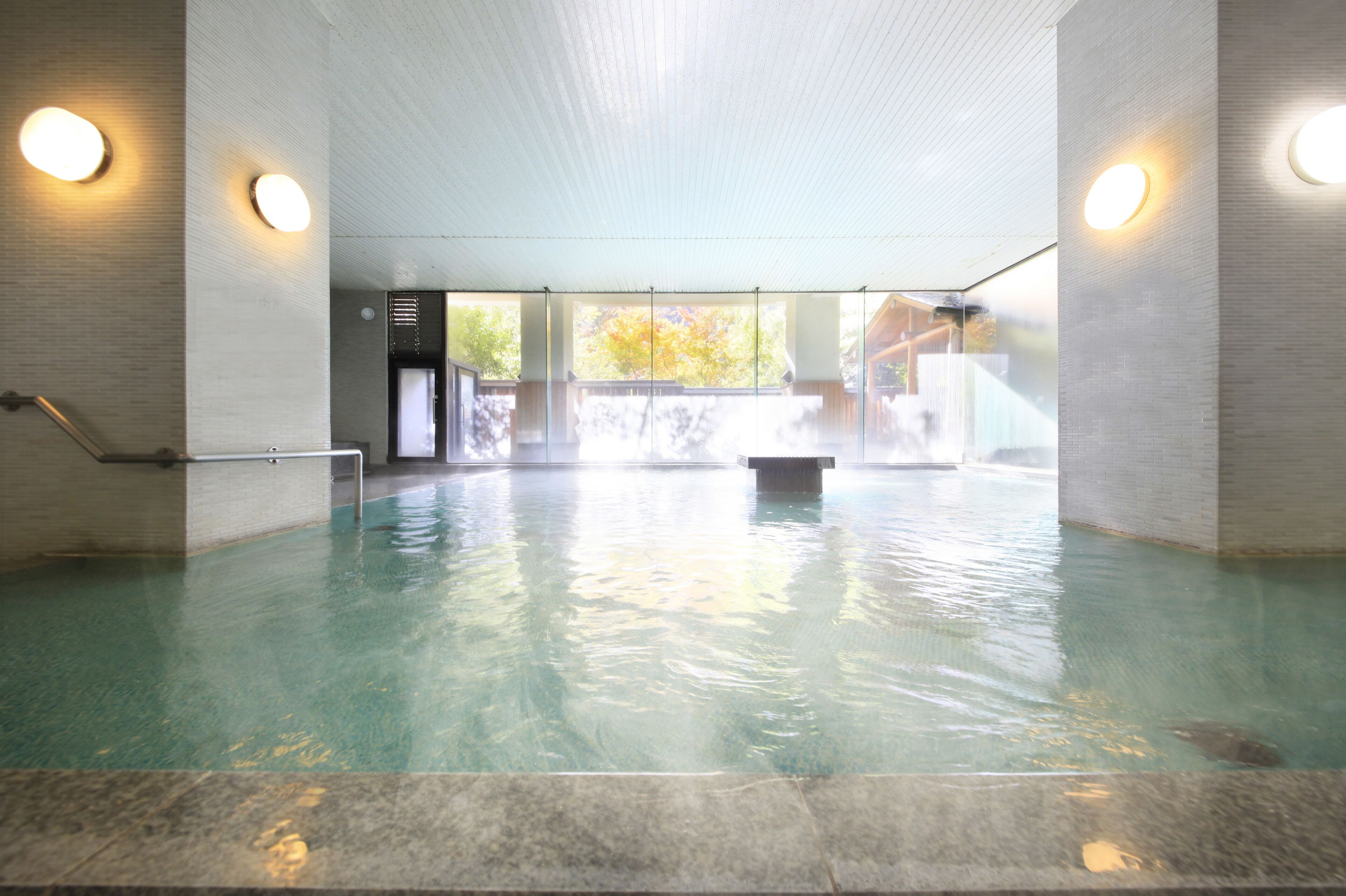 Una piscina interior con agua cristalina, suelo de baldosas y un banco en el centro.