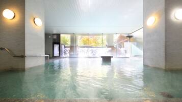 Una piscina interior con agua cristalina, suelo de baldosas y un banco en el centro.