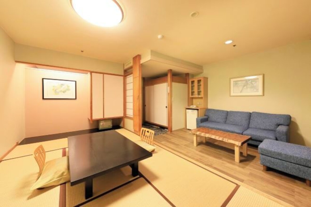 A traditional Japanese-style living room with tatami flooring, a low table, a sofa, and a cabinet.