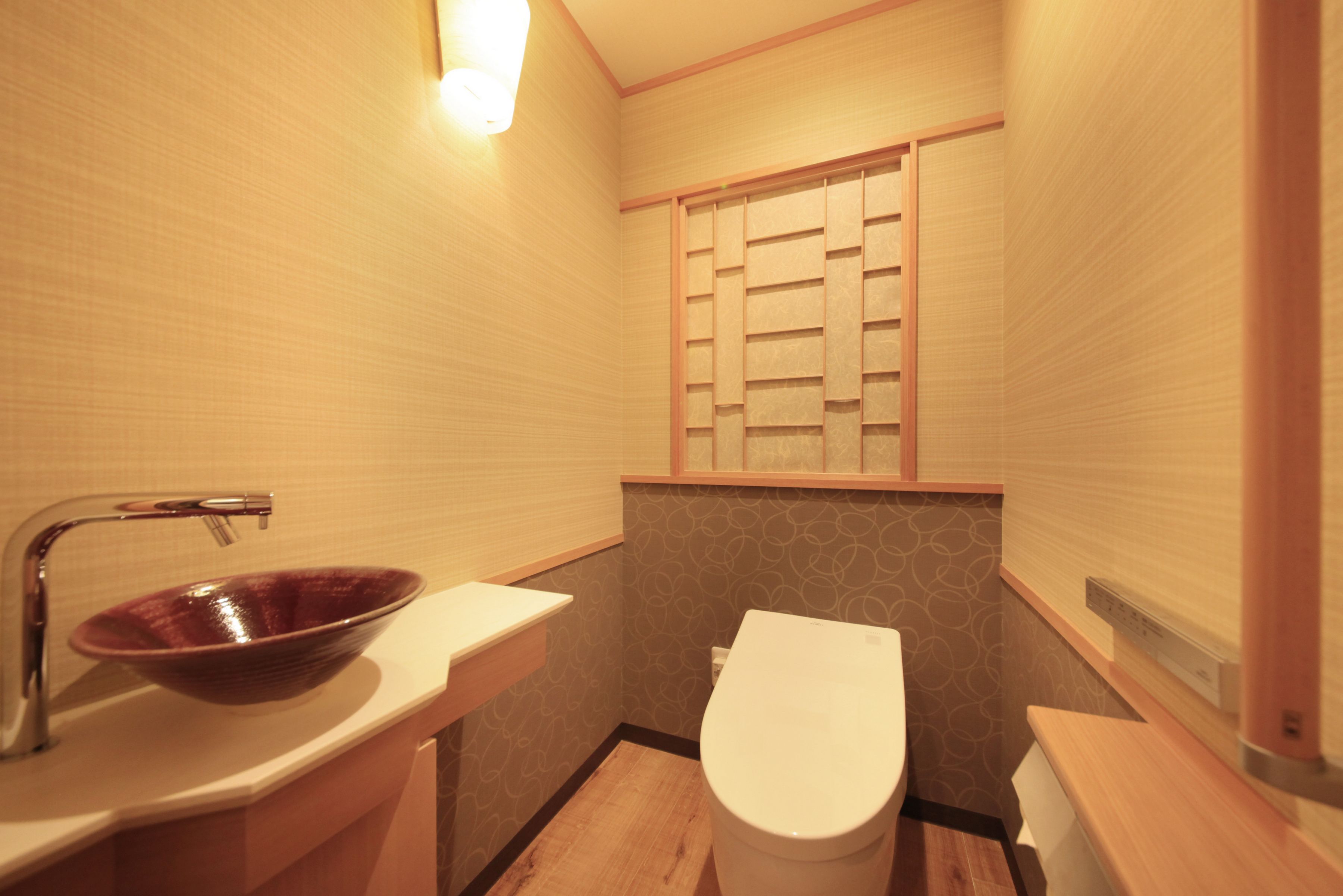 A small bathroom with a wooden vanity, a ceramic sink, a toilet, and a window with a wooden blind.
