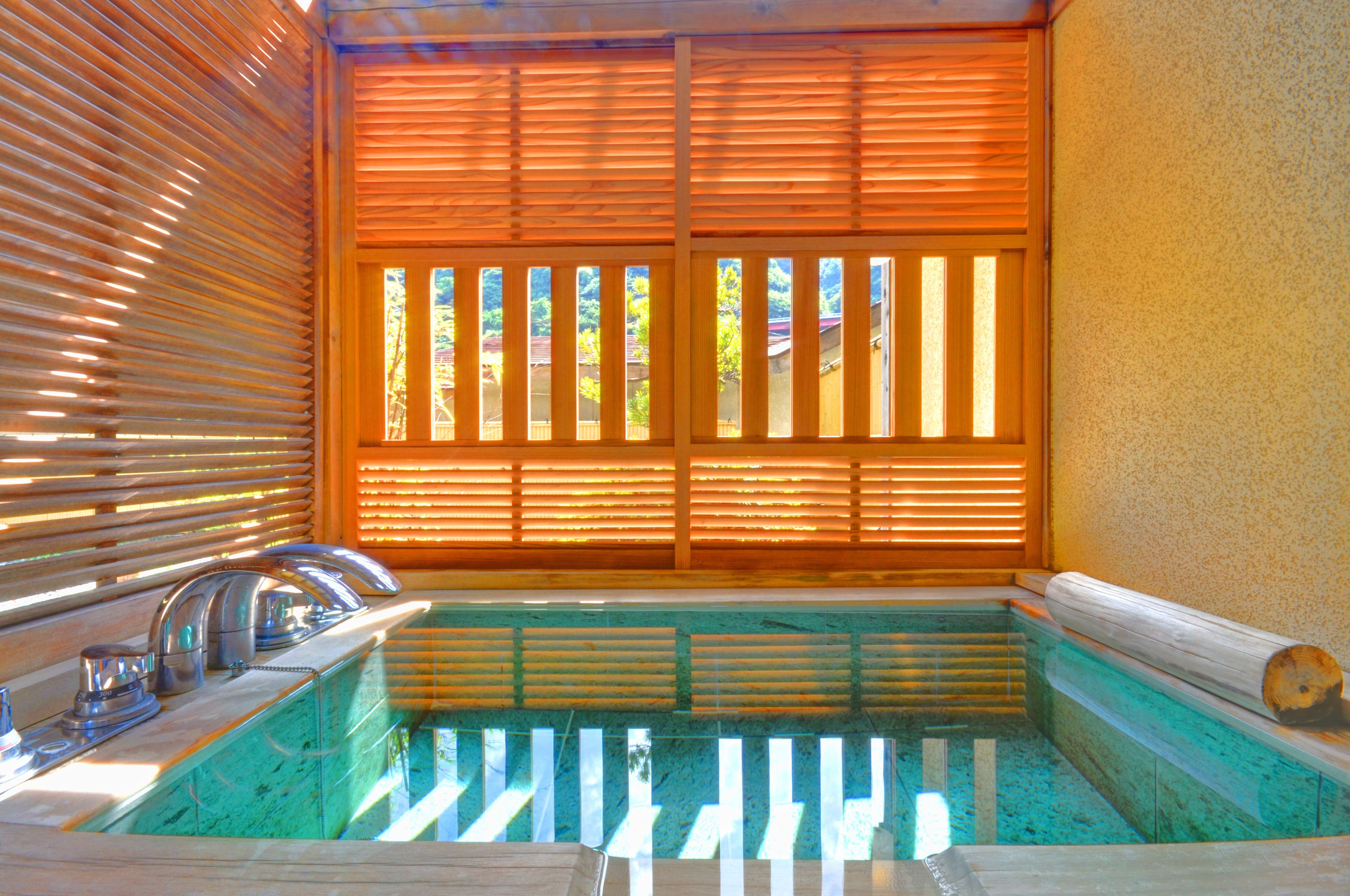 A spa area with a hot tub, wooden blinds, and a view of greenery outside.