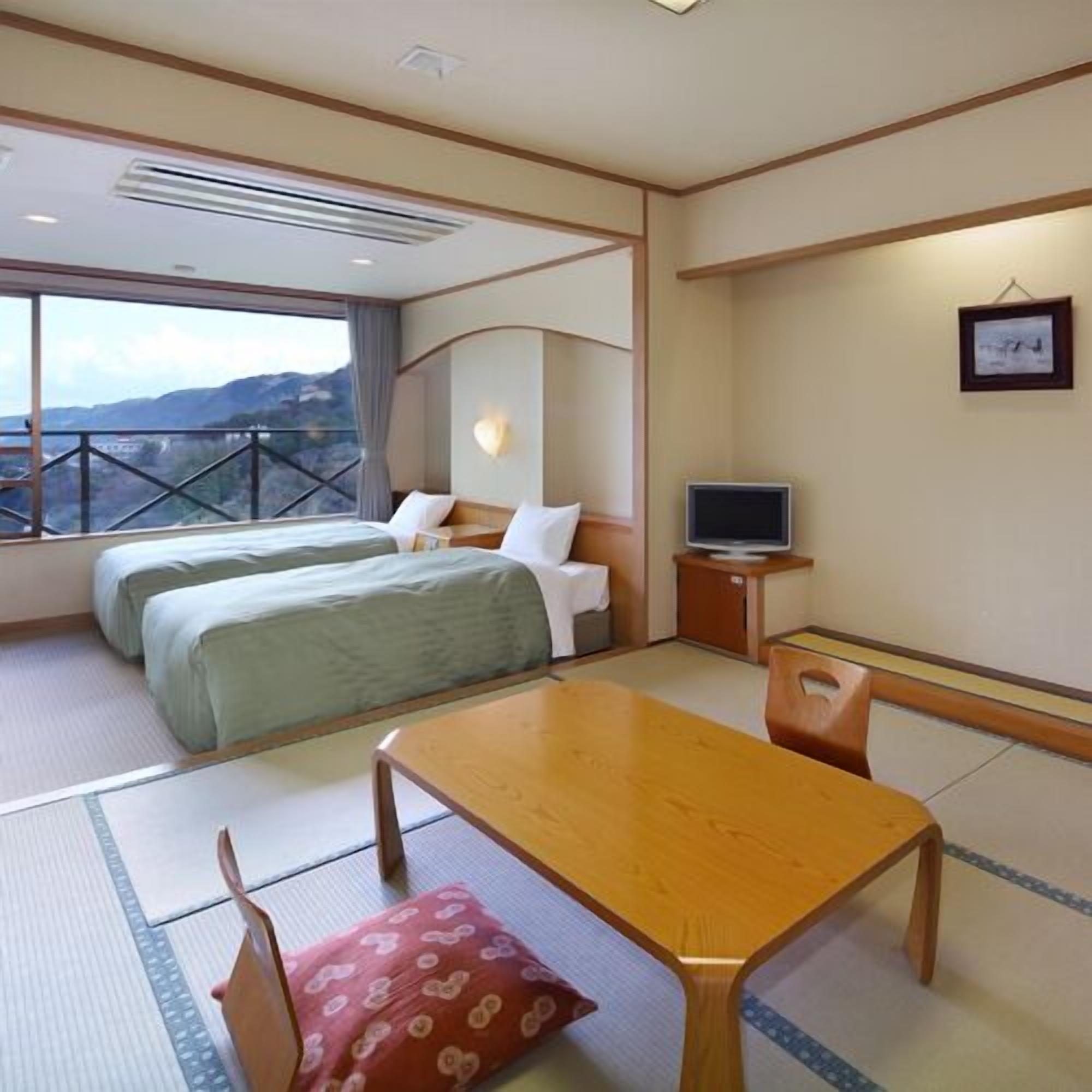 A hotel room with two beds, a TV, a dining table, and a view of mountains.