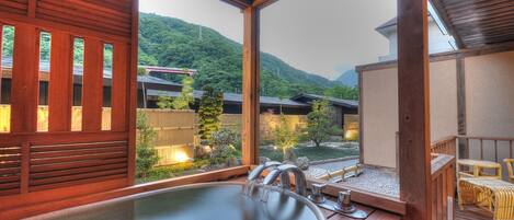 A wooden deck with a hot tub, wooden railings, and a view of a mountainous landscape.