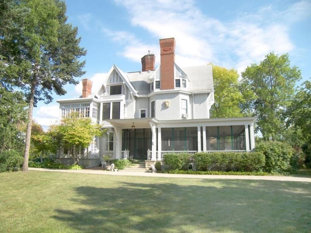 A large, stately house with a prominent front porch, multiple chimneys, and a well-maintained lawn.