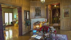A spacious room with wooden paneling, a chandelier, a fireplace, and a large rug. - Alexander Mansion Bed and Breakfast (Winona)